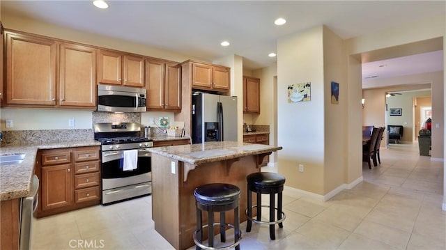 kitchen featuring a kitchen island, appliances with stainless steel finishes, light stone counters, a kitchen bar, and recessed lighting