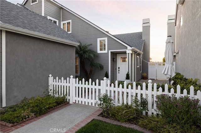 view of front of home with a gate, roof with shingles, a chimney, stucco siding, and a fenced front yard