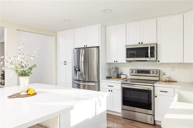 kitchen with wood finished floors, decorative backsplash, light countertops, white cabinets, and appliances with stainless steel finishes