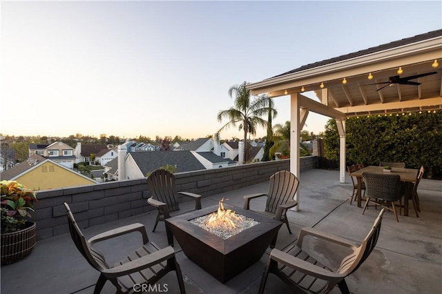 patio terrace at dusk featuring a fire pit, outdoor dining area, and a ceiling fan