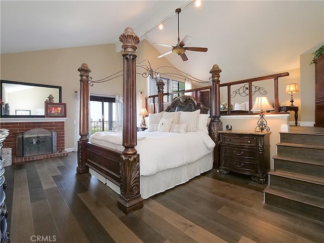 bedroom with dark wood-style floors, a brick fireplace, high vaulted ceiling, and track lighting