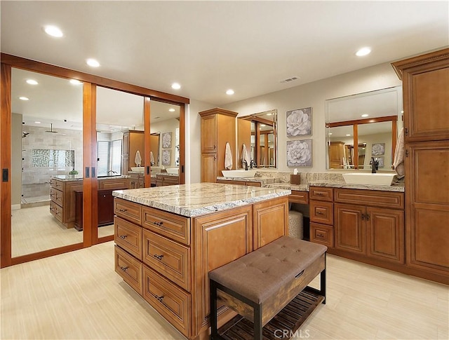 kitchen featuring brown cabinetry, a sink, light stone counters, and a kitchen island