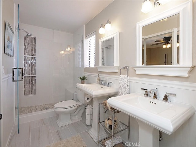 bathroom with toilet, a wainscoted wall, ceiling fan, and tiled shower