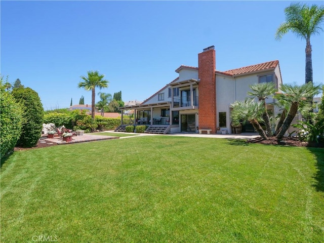 back of property featuring a patio, a balcony, a yard, stucco siding, and a chimney