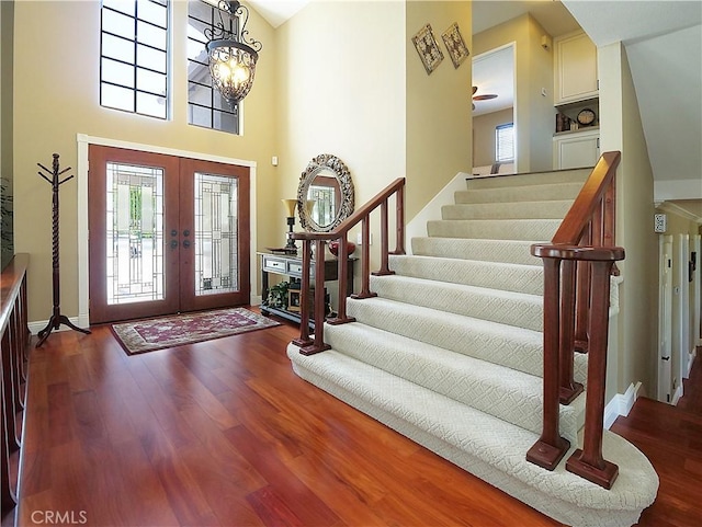 foyer entrance with baseboards, wood finished floors, stairs, a high ceiling, and french doors