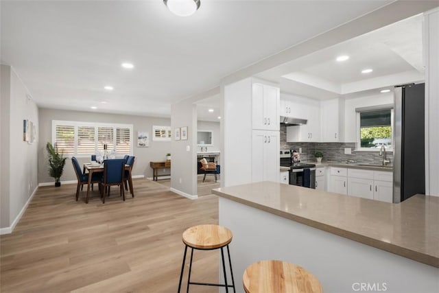 kitchen featuring tasteful backsplash, white cabinets, stainless steel appliances, light wood-type flooring, and under cabinet range hood