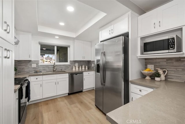 kitchen with a raised ceiling, appliances with stainless steel finishes, a sink, and white cabinets