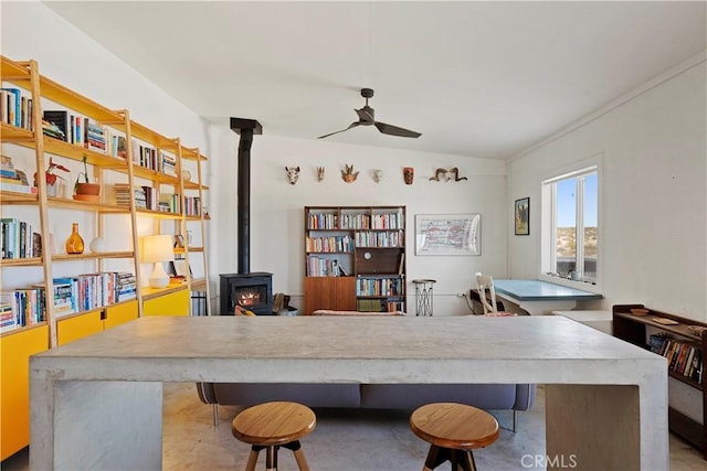 office space featuring a wood stove, ceiling fan, and concrete floors