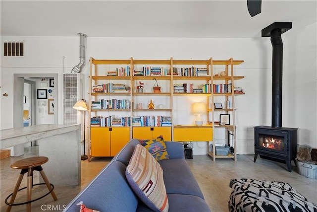 living area featuring a wood stove, visible vents, and finished concrete floors