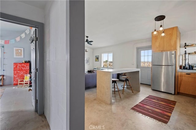 kitchen with concrete flooring, a breakfast bar area, freestanding refrigerator, and decorative light fixtures