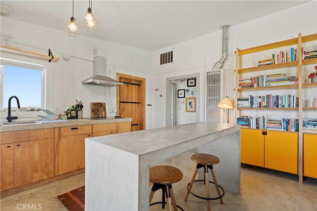 kitchen with decorative light fixtures, light countertops, visible vents, a sink, and wall chimney range hood