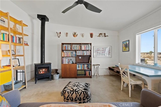 sitting room with a wood stove, ceiling fan, and concrete flooring