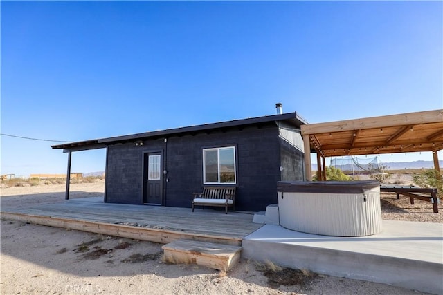 rear view of house with a hot tub and a wooden deck