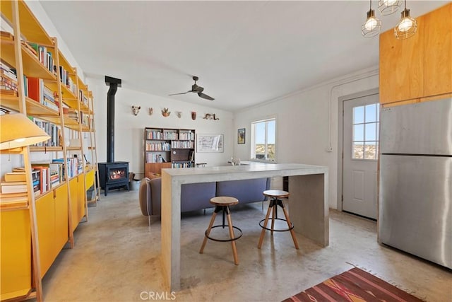 kitchen with a wood stove, finished concrete flooring, a ceiling fan, and freestanding refrigerator