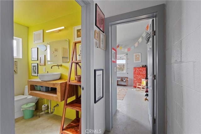 hall with concrete flooring, plenty of natural light, a sink, and concrete block wall