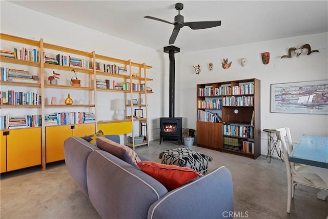 living area with a wood stove, concrete floors, and a ceiling fan