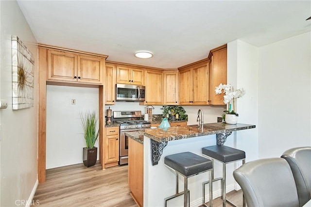 kitchen featuring dark stone counters, light wood-style flooring, appliances with stainless steel finishes, a kitchen breakfast bar, and a peninsula