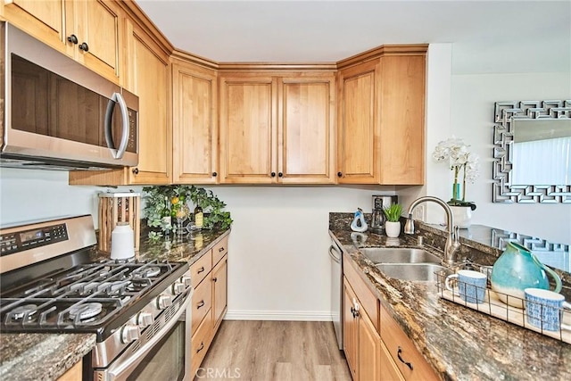 kitchen with light wood-type flooring, dark stone countertops, stainless steel appliances, and a sink