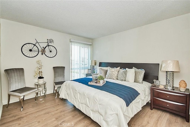 bedroom with a textured ceiling, baseboards, and light wood-style floors