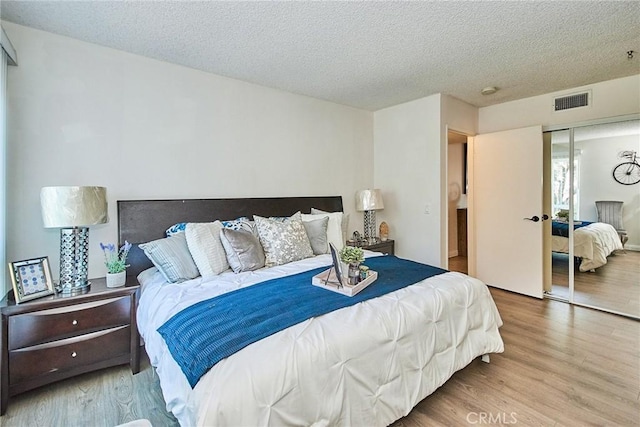 bedroom featuring a textured ceiling, a closet, wood finished floors, and visible vents