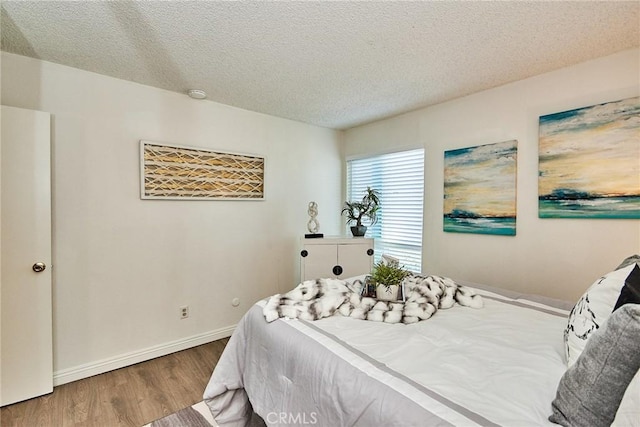 bedroom featuring a textured ceiling, baseboards, and wood finished floors