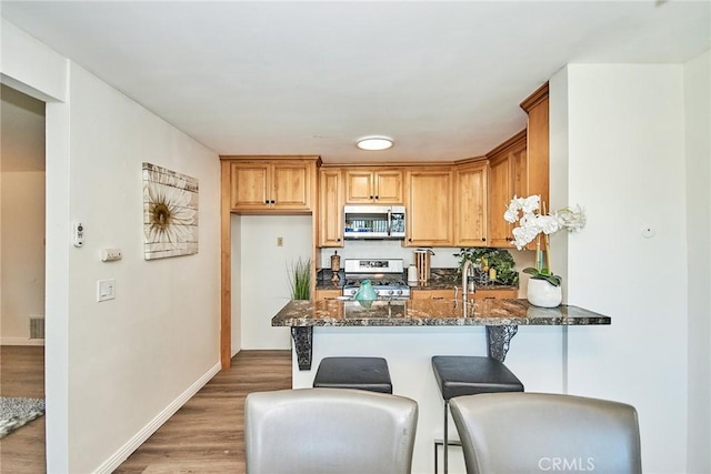 kitchen featuring light wood-style flooring, stainless steel appliances, a peninsula, baseboards, and dark stone counters