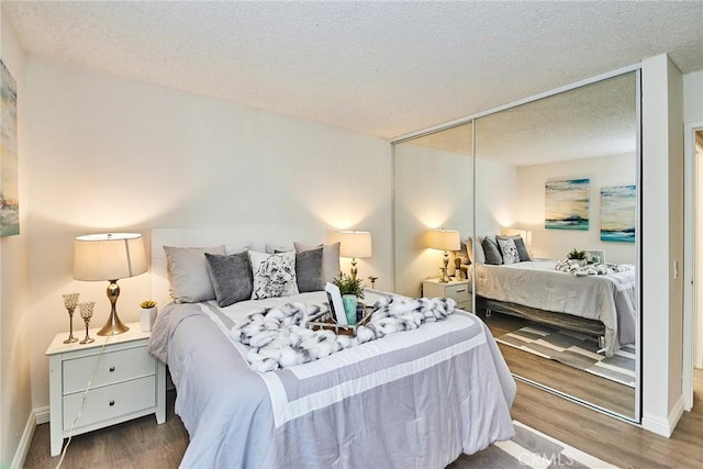 bedroom with a closet, a textured ceiling, baseboards, and wood finished floors