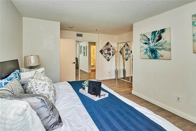 bedroom with a textured ceiling, wood finished floors, visible vents, and baseboards