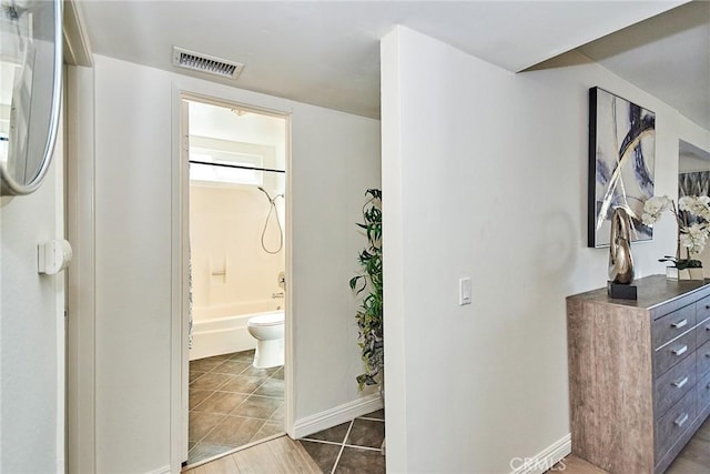 interior space featuring baseboards, visible vents, toilet, tile patterned floors, and washtub / shower combination