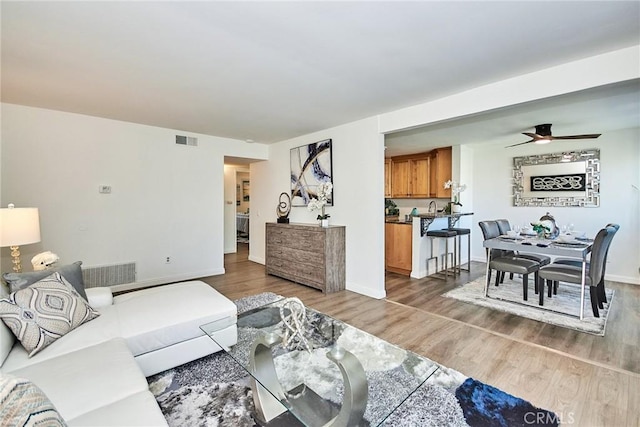 living room featuring ceiling fan, wood finished floors, visible vents, and baseboards