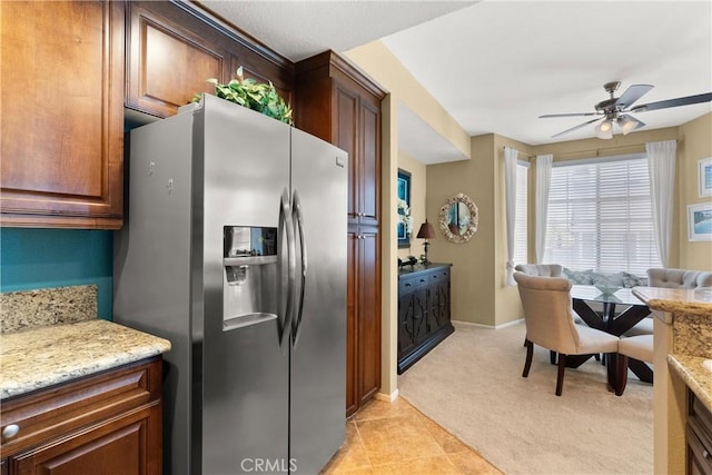 kitchen featuring stainless steel refrigerator with ice dispenser, light colored carpet, a ceiling fan, light stone countertops, and baseboards