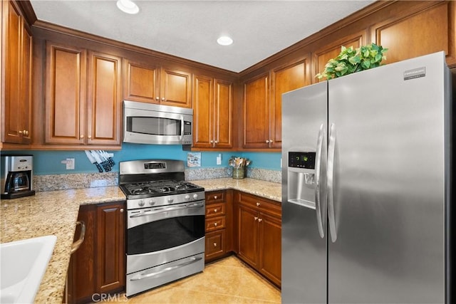 kitchen featuring light stone counters, stainless steel appliances, brown cabinetry, light tile patterned flooring, and a sink