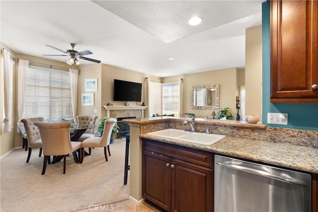 kitchen with a tiled fireplace, light colored carpet, a peninsula, stainless steel dishwasher, and a sink