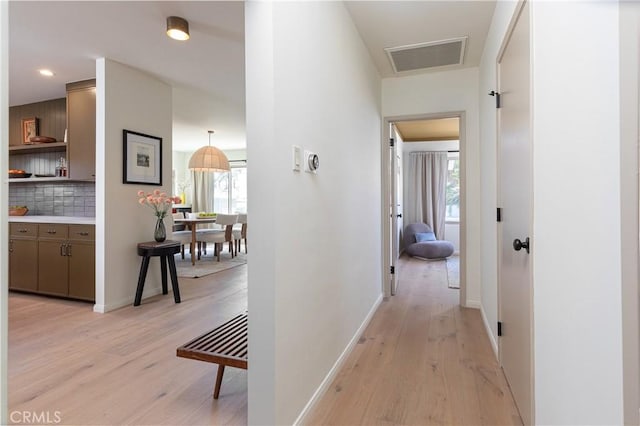 corridor featuring light wood finished floors, plenty of natural light, visible vents, and baseboards