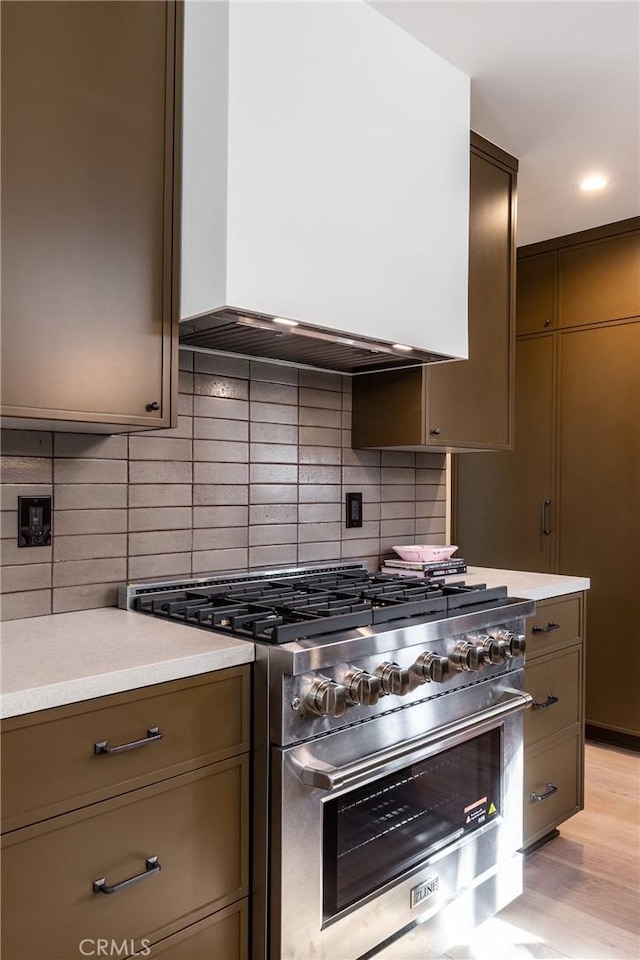 kitchen featuring light wood-style floors, tasteful backsplash, high end range, and light countertops