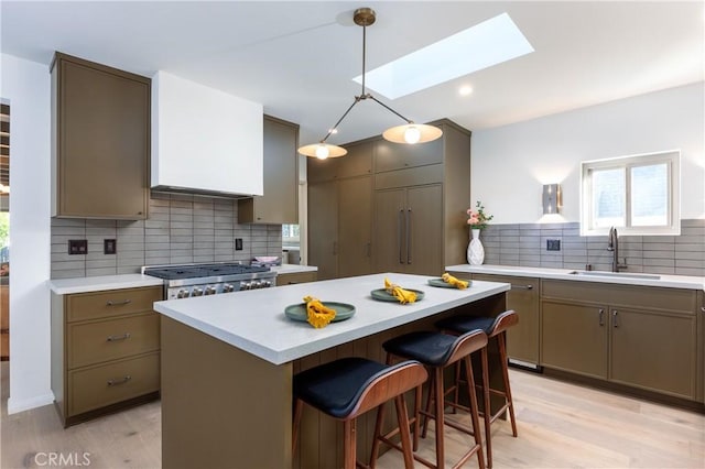 kitchen with a skylight, light countertops, backsplash, a sink, and range