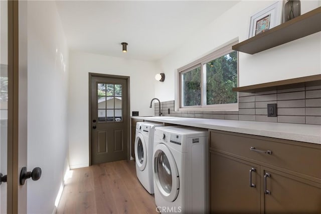 laundry area featuring cabinet space, a sink, light wood finished floors, and separate washer and dryer