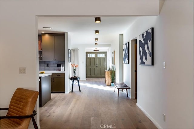 interior space with visible vents, light countertops, backsplash, light wood-type flooring, and baseboards