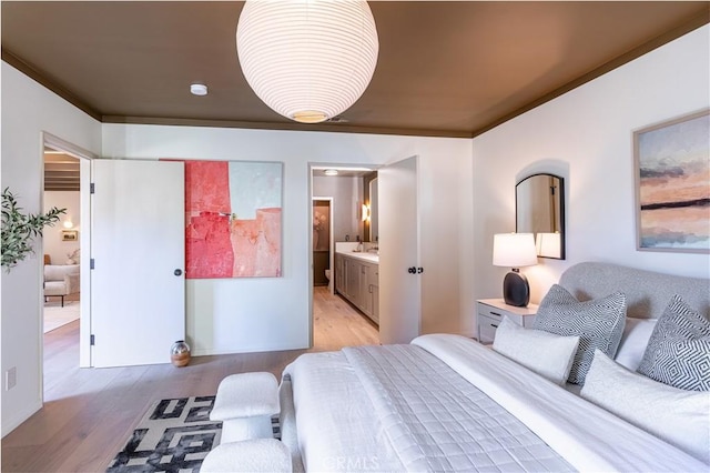 bedroom featuring ornamental molding, light wood-type flooring, and connected bathroom