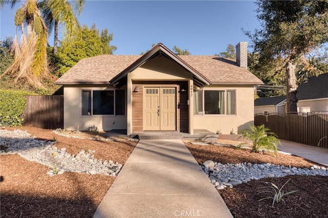 bungalow-style home featuring a chimney, stucco siding, a shingled roof, a gate, and fence