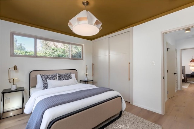 bedroom featuring light wood-type flooring, baseboards, and a closet