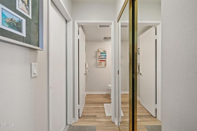 hall with visible vents, light wood-style flooring, and baseboards