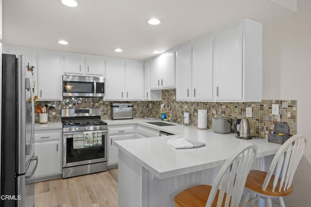 kitchen featuring light wood-style flooring, stainless steel appliances, a peninsula, a sink, and light countertops