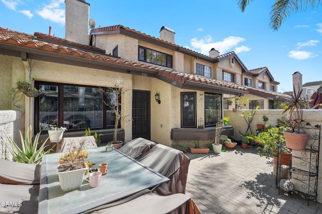 back of property with a tile roof, a patio, a chimney, and stucco siding