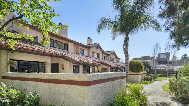 exterior space featuring stucco siding, a chimney, fence, and a tiled roof