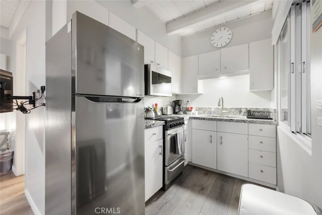 kitchen with beam ceiling, stainless steel appliances, white cabinets, a sink, and wood finished floors