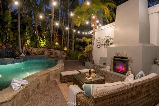 pool at twilight featuring an outdoor living space with a fireplace, a patio area, and an outdoor pool