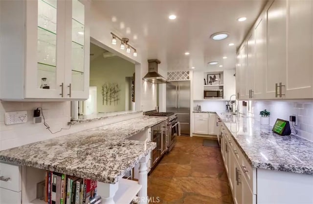 kitchen with white cabinets, appliances with stainless steel finishes, light stone counters, range hood, and open shelves