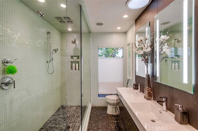 full bathroom featuring a sink, a tile shower, toilet, and double vanity