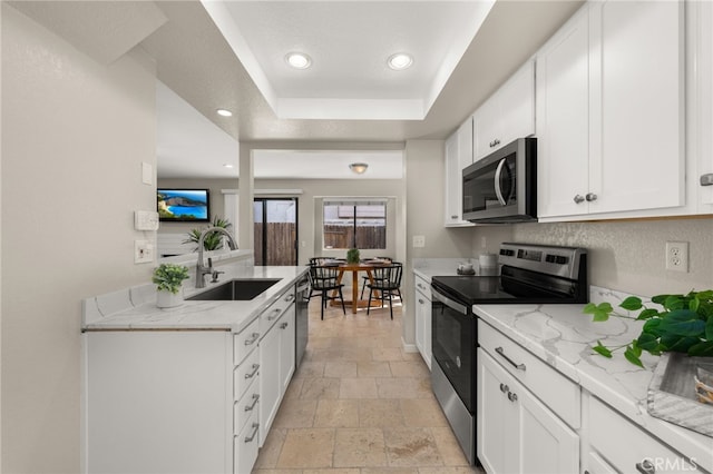 kitchen featuring stainless steel appliances, stone tile flooring, a raised ceiling, white cabinetry, and a sink